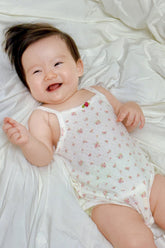 Happy baby wearing Avauma Summer Picot Sleeveless Bodysuit Rosebell. Infant lying down, laughing in a white romper with pink floral print.